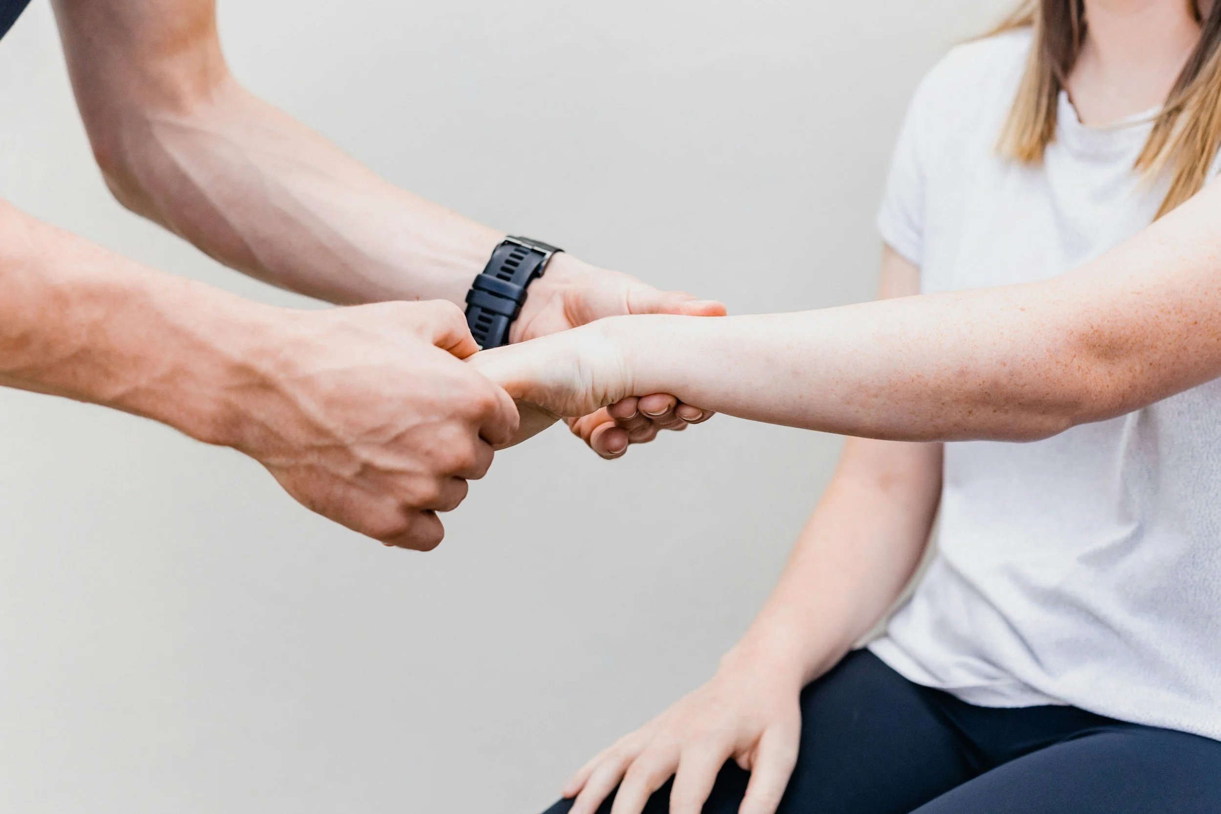 Two people are holding hands in a handshake, with one person's hand resting on the other's arm, against a white background.