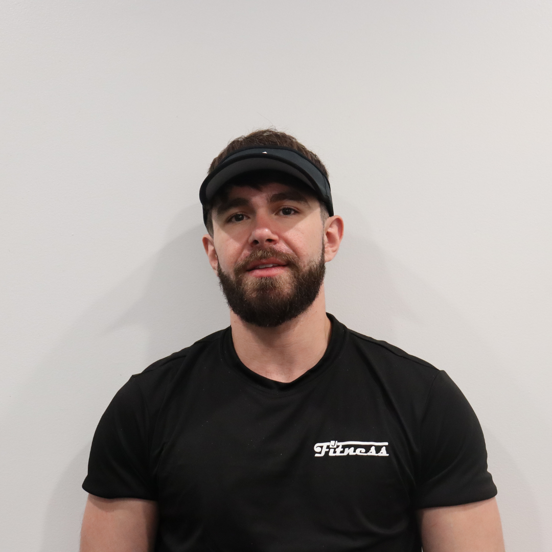Man with beard wearing black T-shirt with 'Fincas' logo and black visor cap, sitting against a plain white wall.