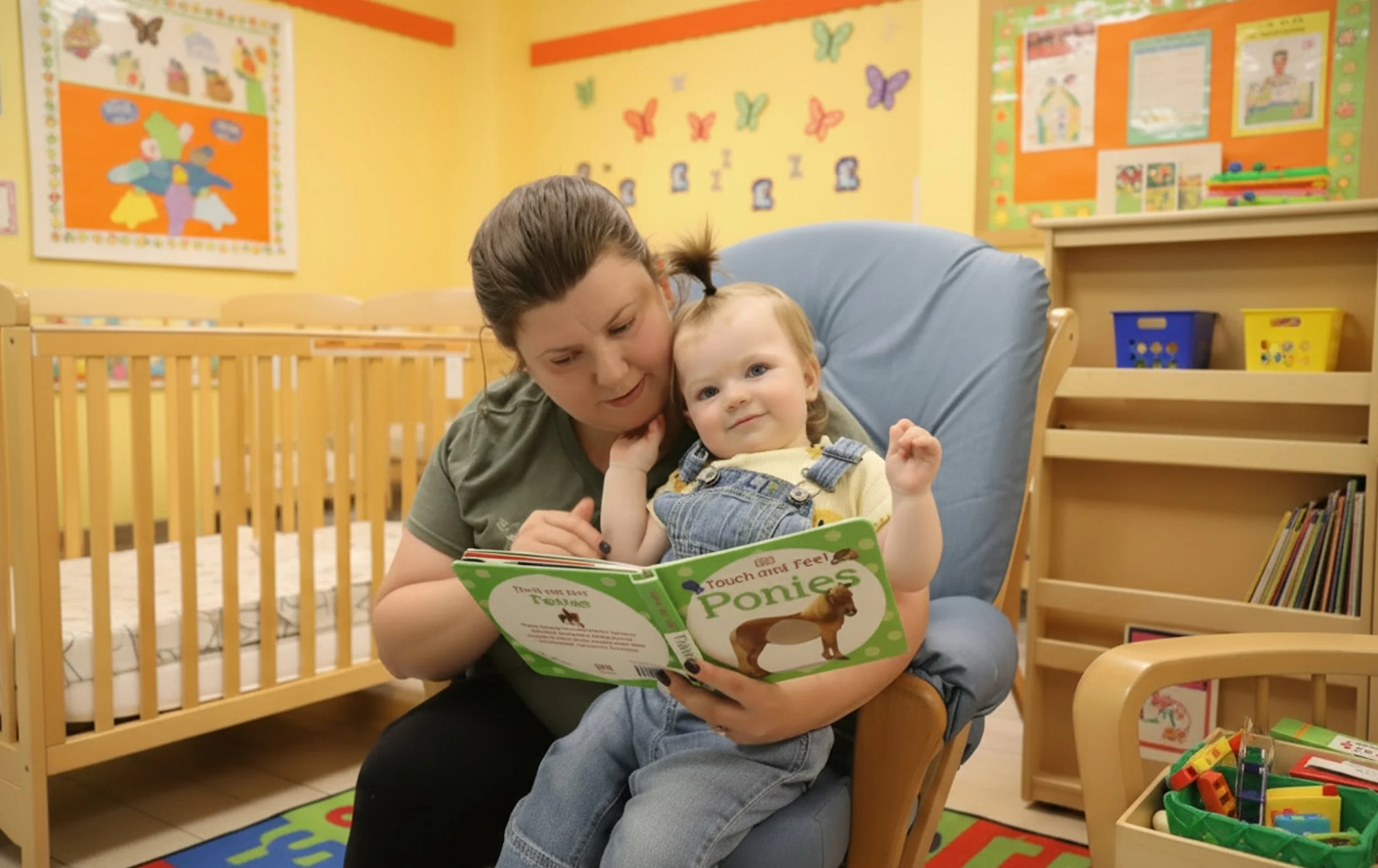 A woman and a young child sitting in a colorful, child-friendly room, reading a book titled 'Touch and Feel Ponies.' The room has yellow walls decorated with butterfly posters, a wooden crib, and bookshelves filled with children's books and toys.
