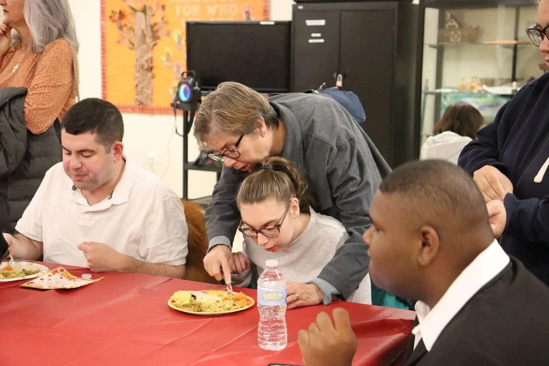 A woman is helping a young girl cut her food at a table during a social gathering.