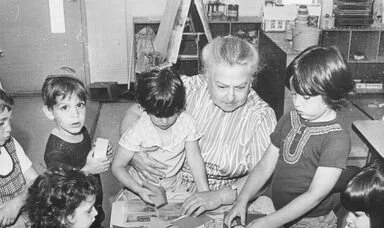 A teacher or adult woman surrounded by young children in a classroom setting.