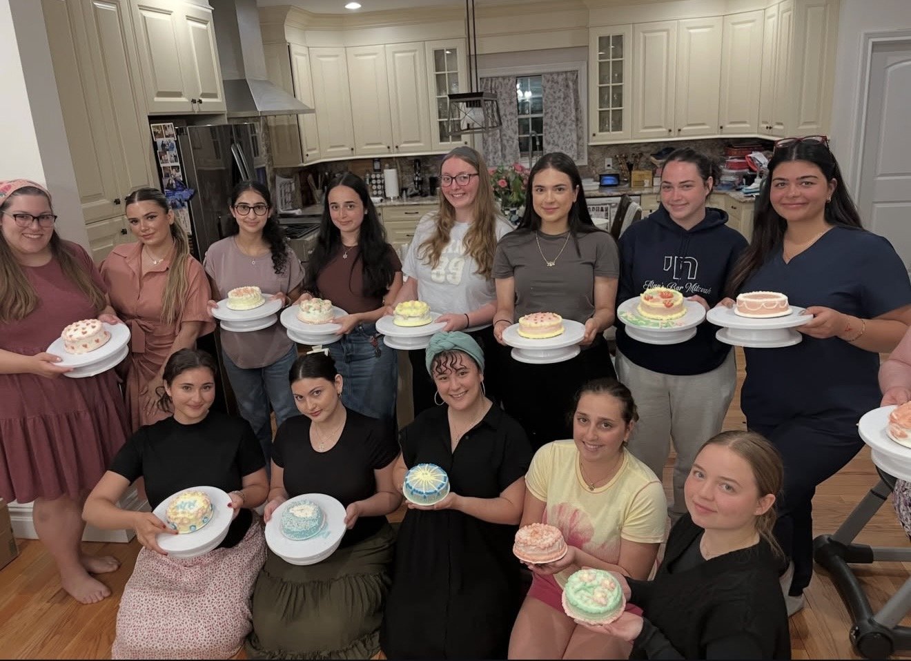 Group of women and girls holding decorated cakes in a kitchen