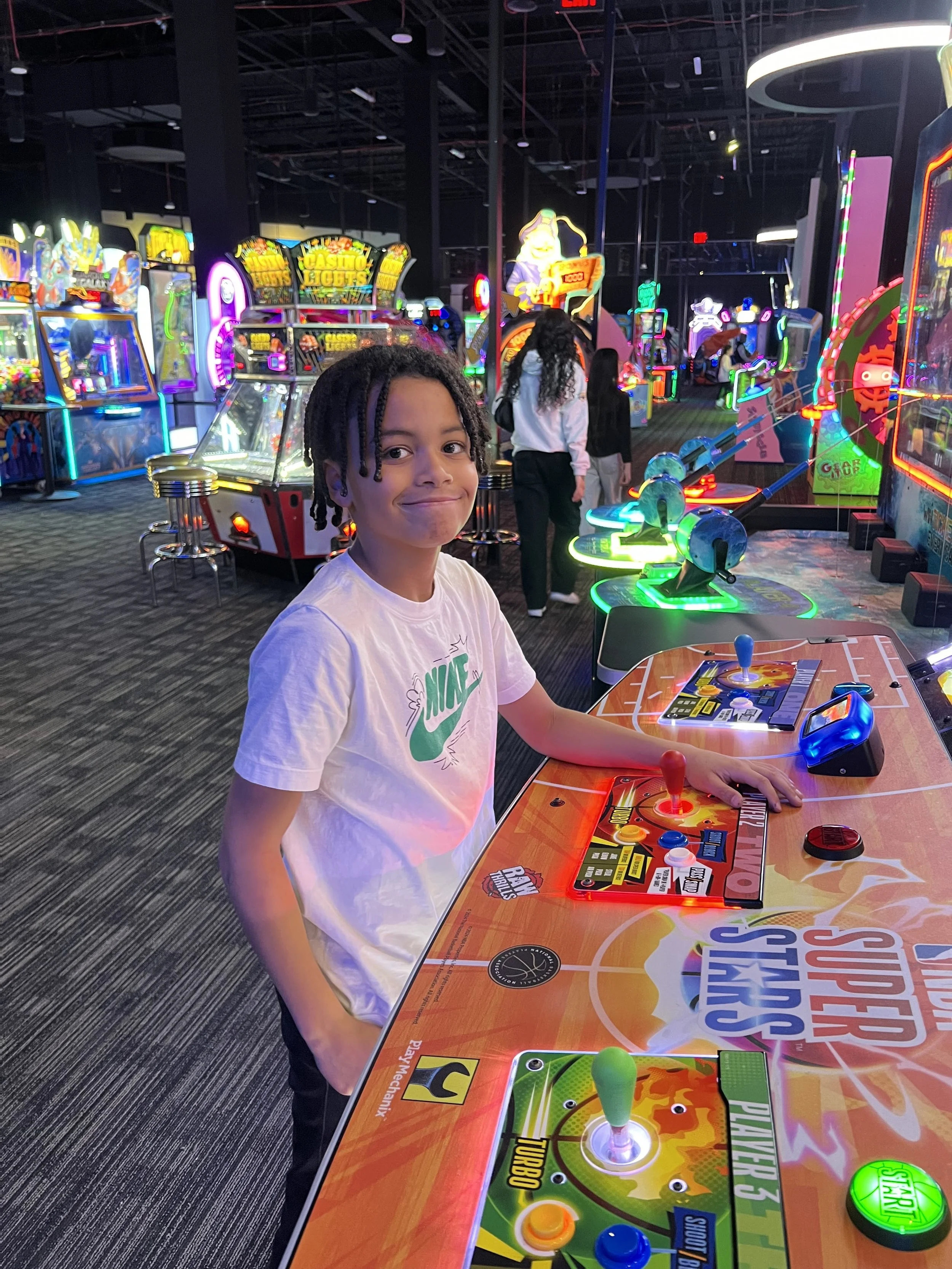 Person playing arcade baseball game at an arcade with various bright neon lights and arcade machines in the background.