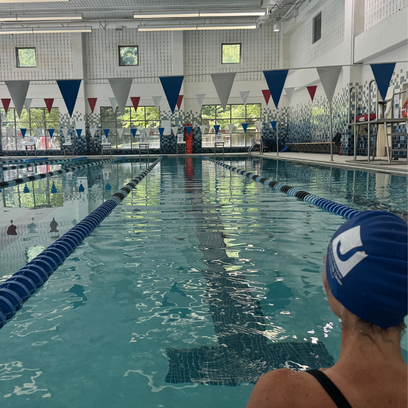 Indoor swimming pool with lane ropes, swimming flags, and a swimmer with a blue Nike swim cap in the foreground.