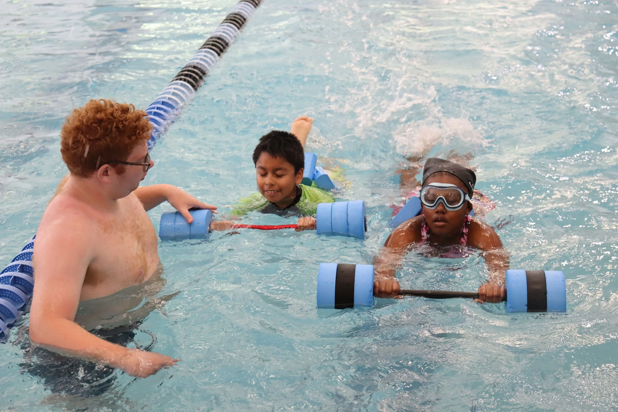 An instructor helping two children with swimming in a pool, with a lane divider visible.