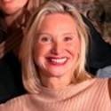A woman with shoulder-length blonde hair, smiling widely, wearing a peach-colored top.