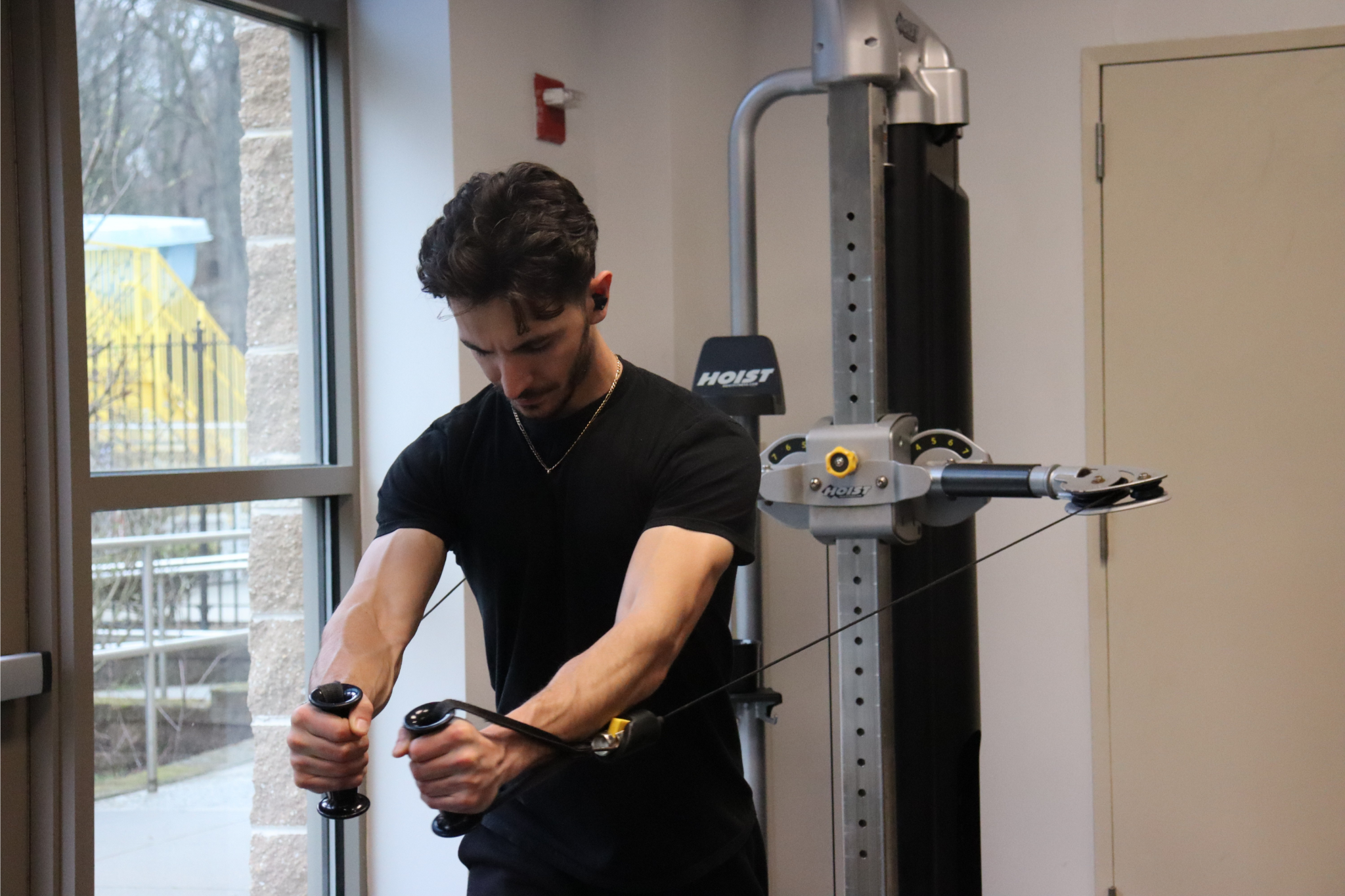 A man working out with resistance bands in a gym near a window.