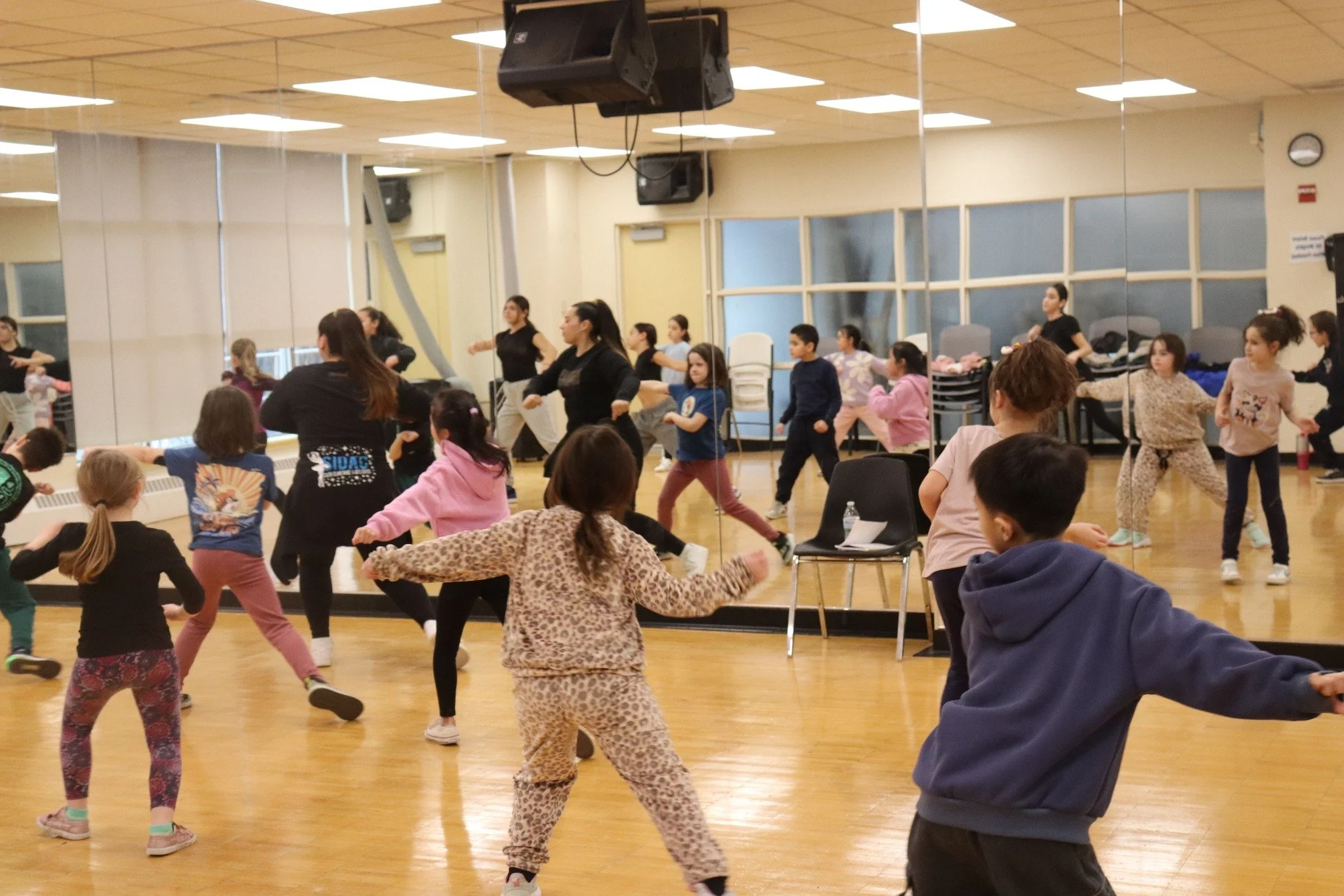 Children and adults participating in a dance class in a dance studio with a large mirror and wooden floor.