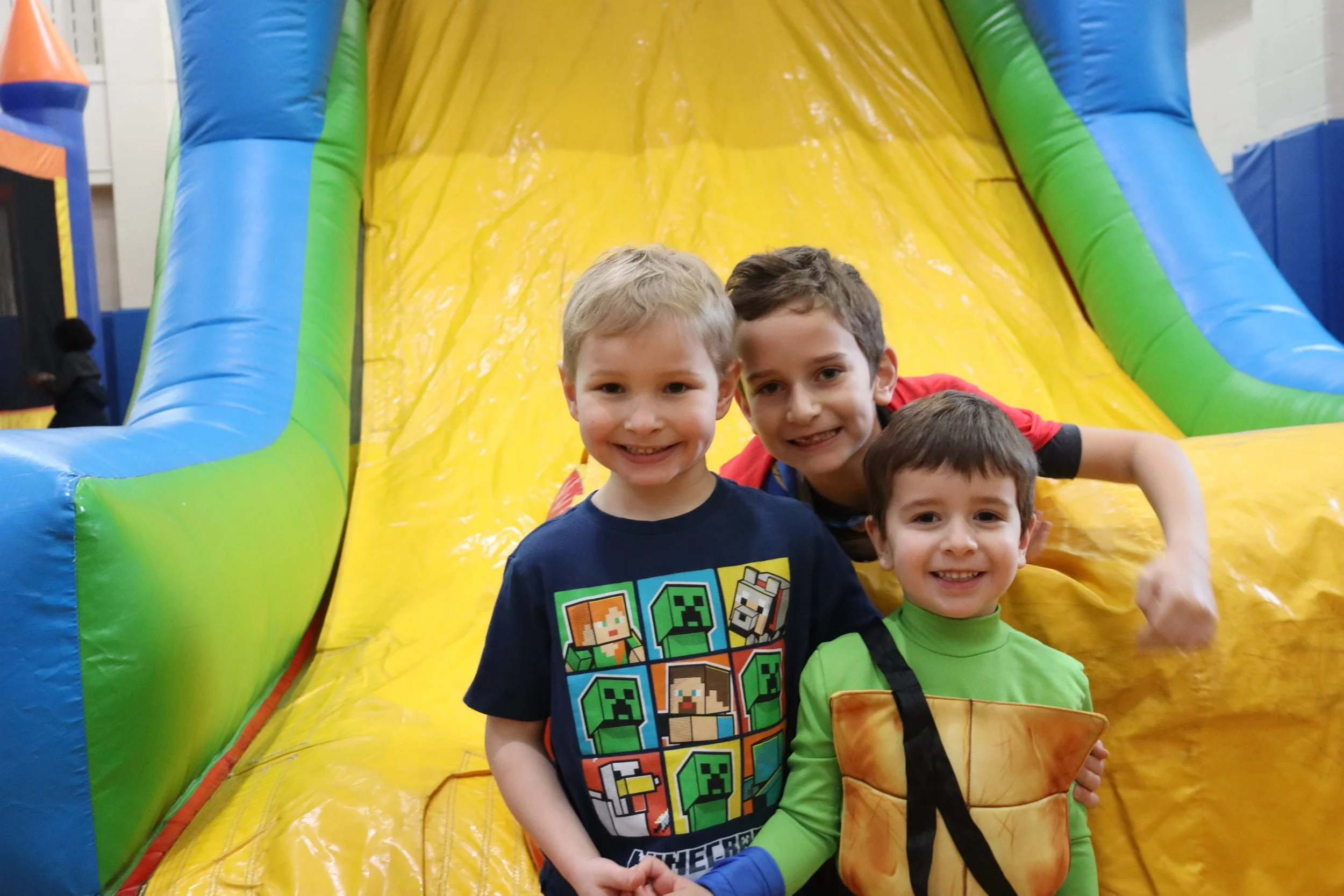 Three young boys smiling and posing in front of an inflatable slide at an indoor play area.