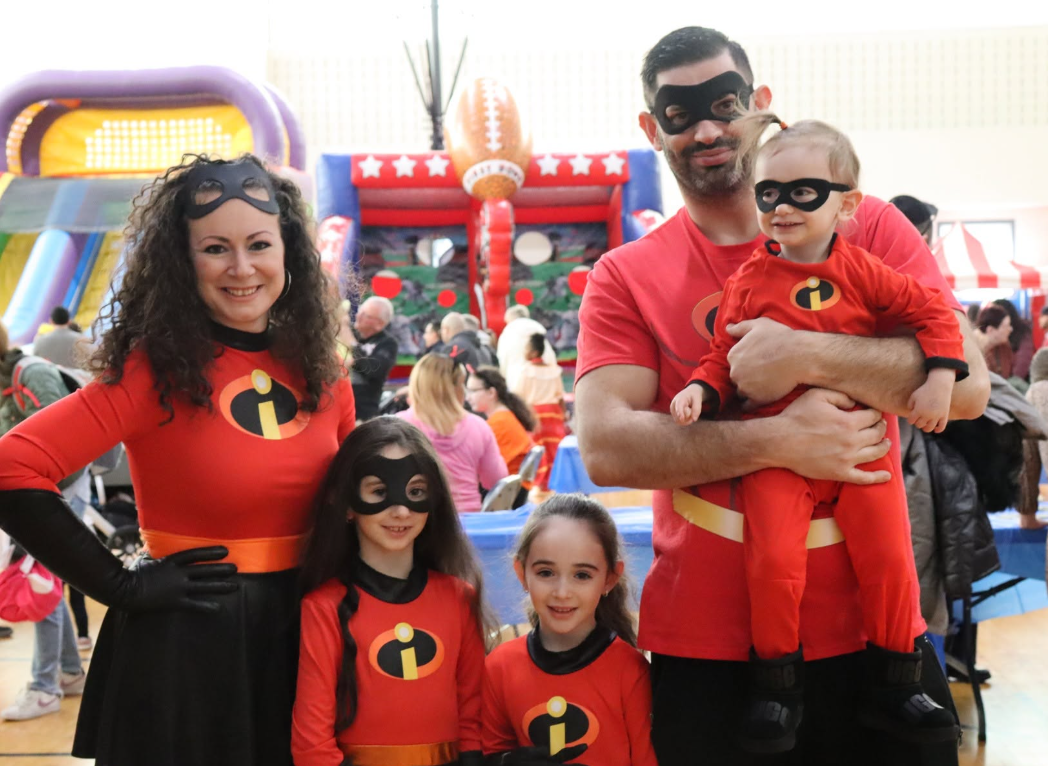 Family dressed as the Incredibles at an indoor event, with children and adults in red and black superhero costumes.