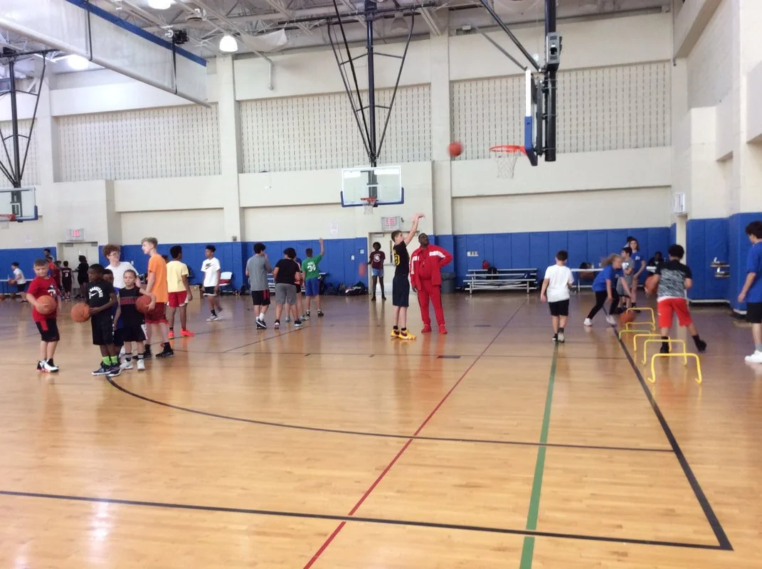Children participating in drills and practicing basketball shots in an indoor gymnasium.