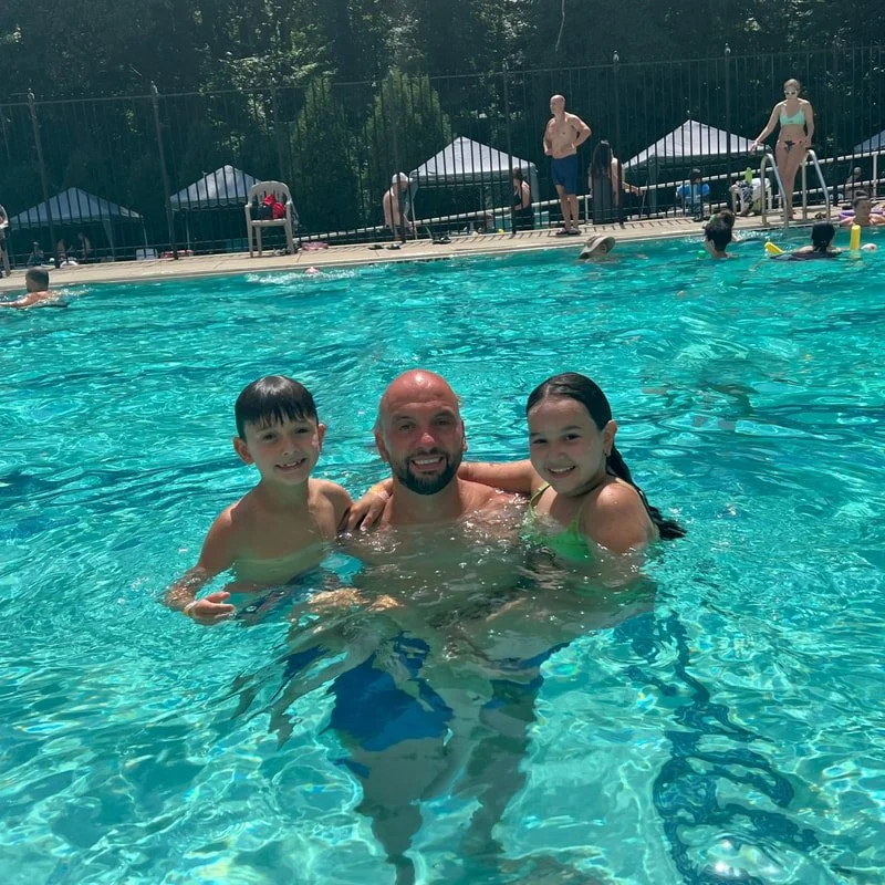 A man with two children in a swimming pool, smiling and posing for a photo.