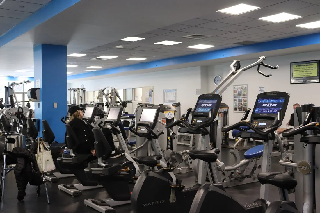 Indoor gym with exercise equipment, including stationary bikes and treadmills, and a person working out.