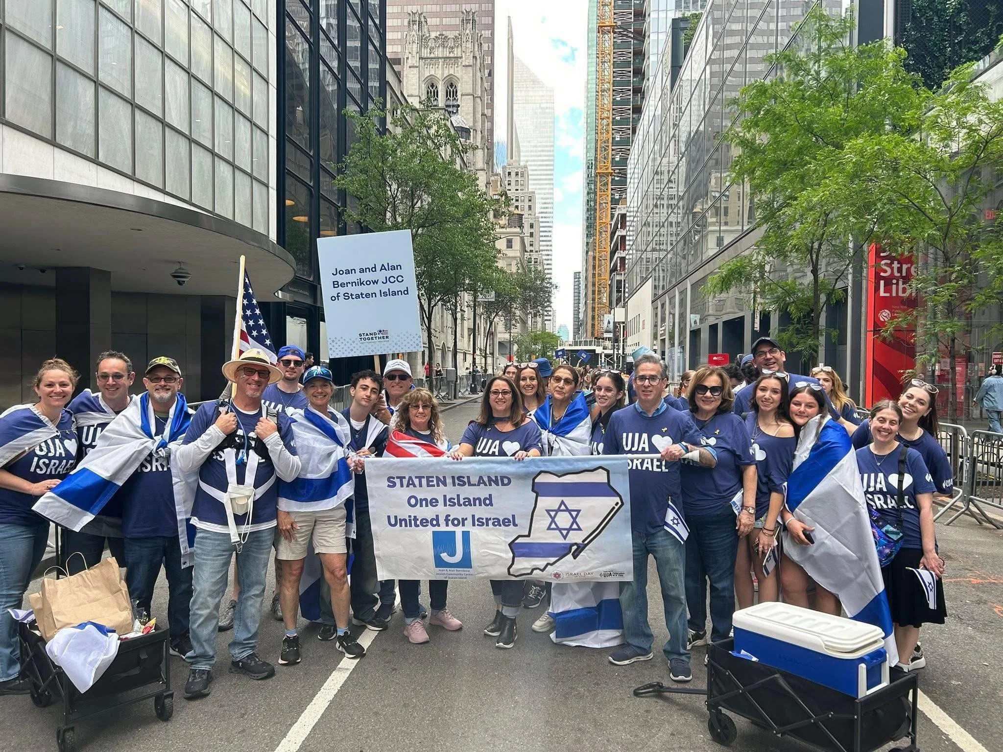 A group of people gathered on a city street holding signs that support Israel and unity for Israel, with tall buildings surrounding them.