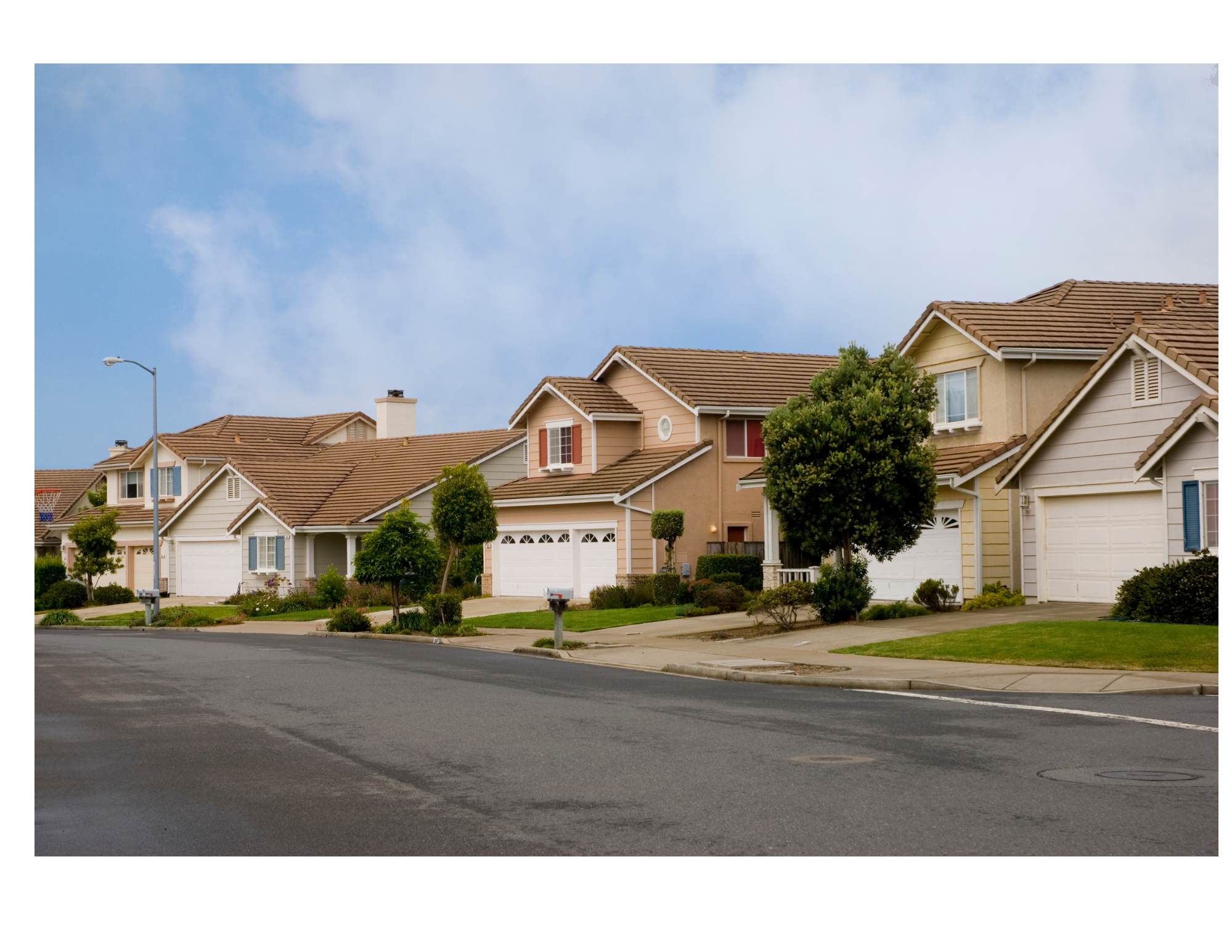 Suburban street view with row of houses, green trees, and blue sky.