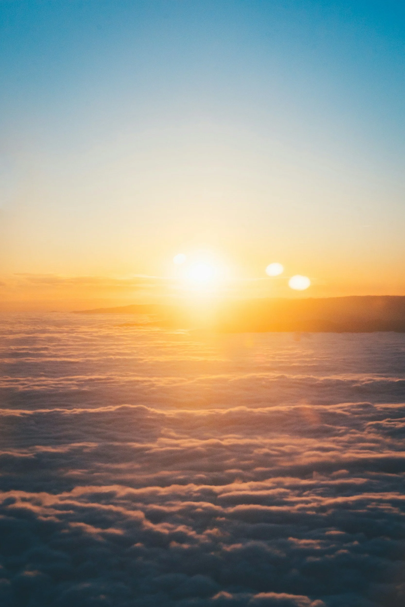 Sun setting over a layer of clouds with a clear blue sky above.