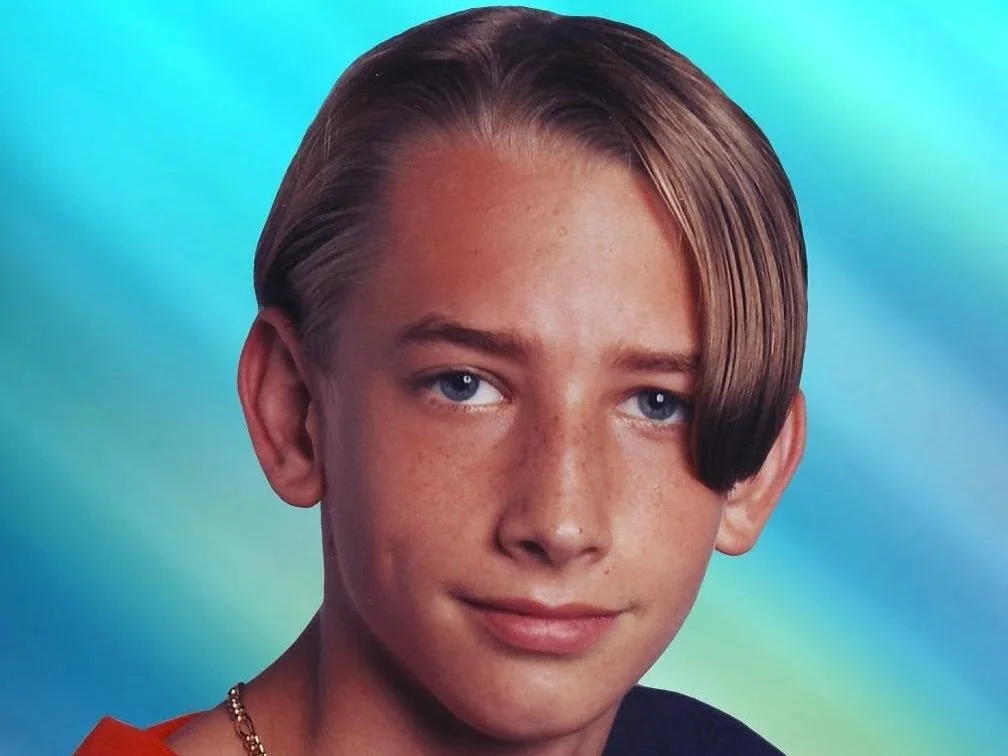 Close-up portrait of a handsome young person with short, straight hair, blue eyes, and a light complexion with freckles, against a colorful blurred background. Brice Williams ; Brice A. Williams. Coach Brice Williams.