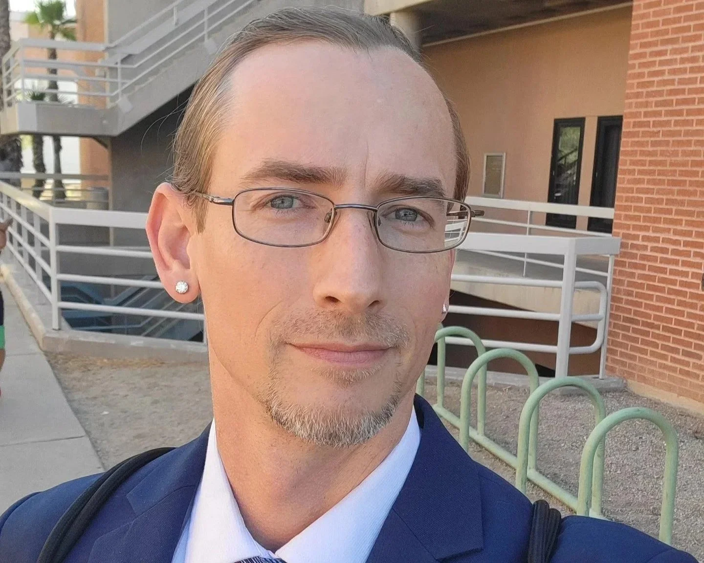 A man with glasses and earrings taking a selfie outside a building with brick and concrete walls. Brice Williams ; Brice A. Williams ; Coach Brice Williams. Professor