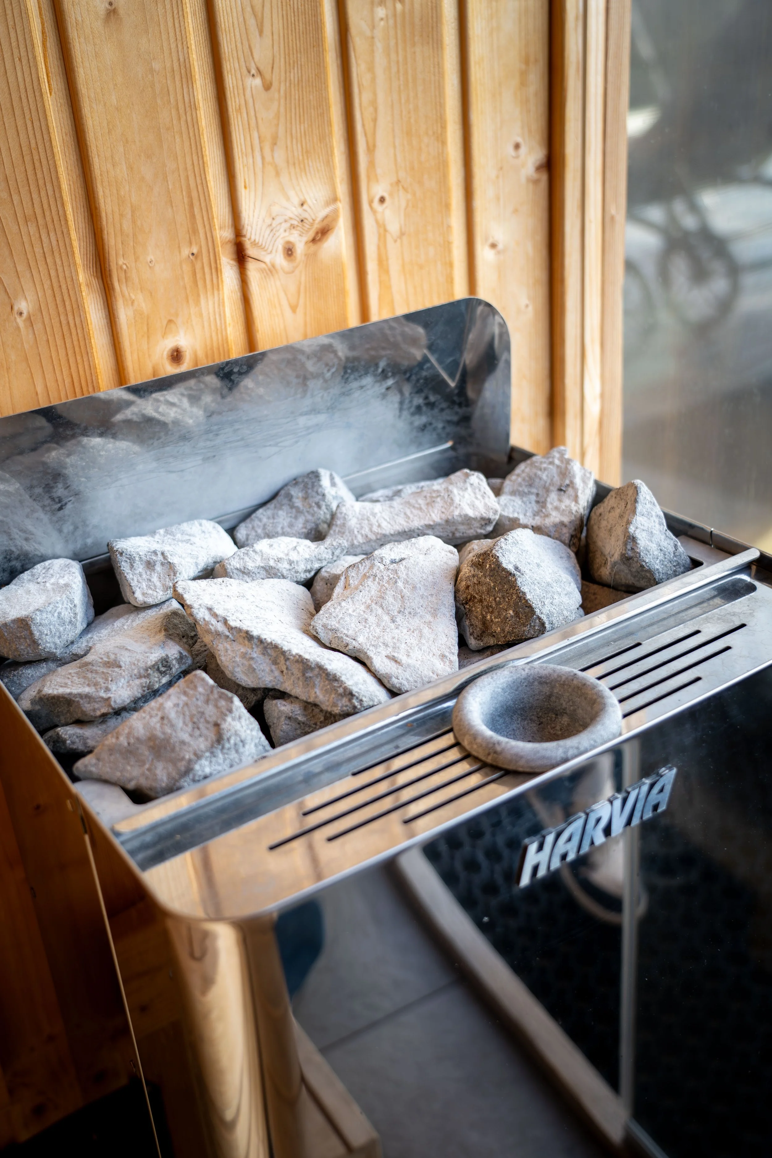Steingrill mit Lava- und Steinen, Holzverkleidung im Hintergrund, Edelstahlrahmen, Teil eines Grillsystems.