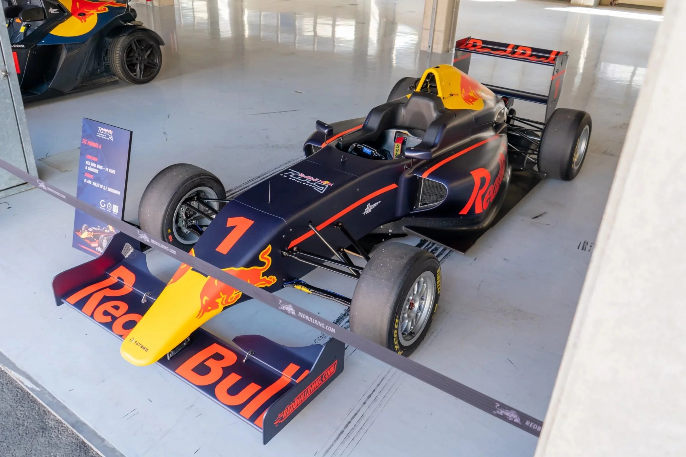 Formel-1-Rennwagen in den Farben Schwarz, Rot und Gelb mit Red Bull-Logo, ausgestellt in einem Raum.