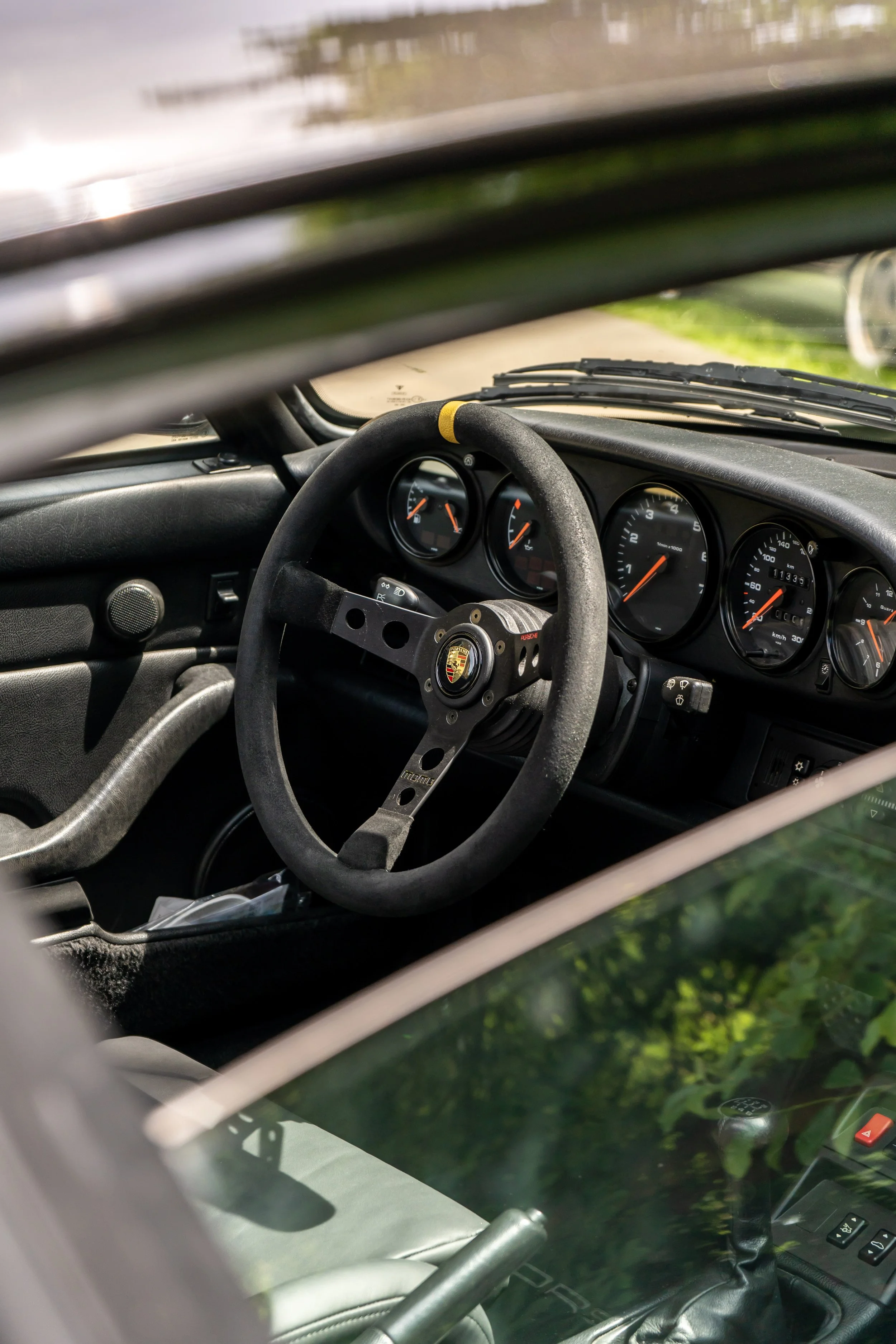 Innenraum eines Autos, Blick auf das Lenkrad und das Tachometer, umgeben von Teilen der Fenster und der Tür.