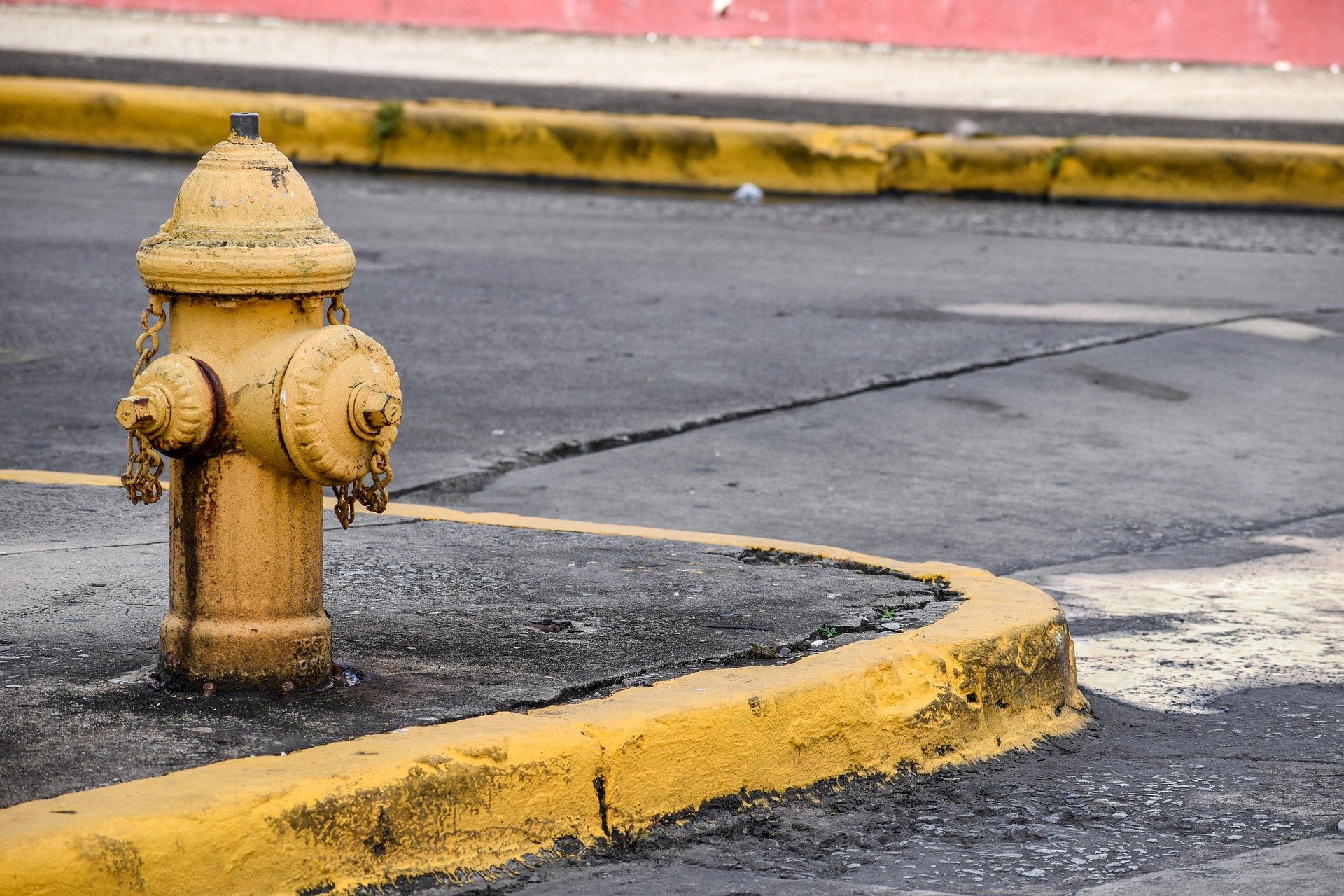 Yellow fire hydrant on a paved street with curb and sidewalk in the background.