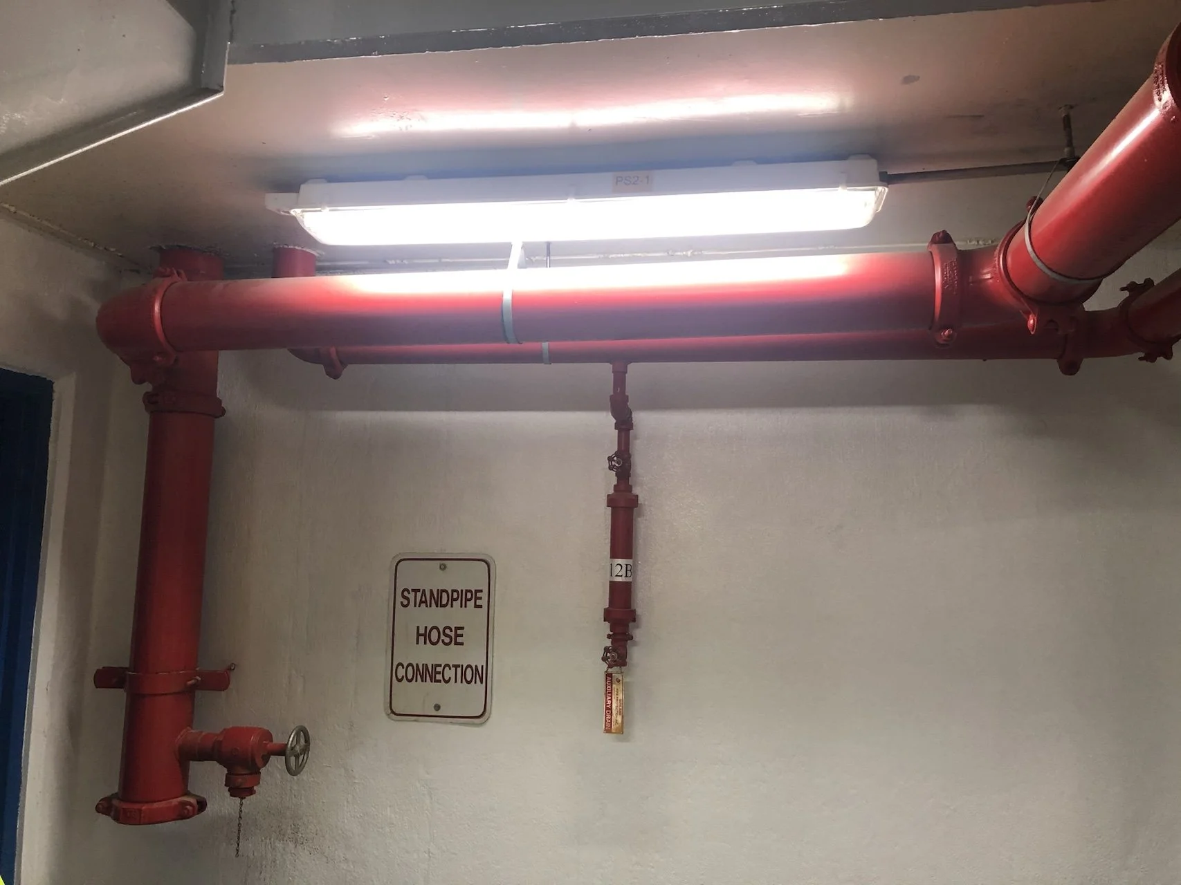 Red fire standpipe pipe system with a clearance light above and a 'Standpipe Hose Connection' sign on the wall