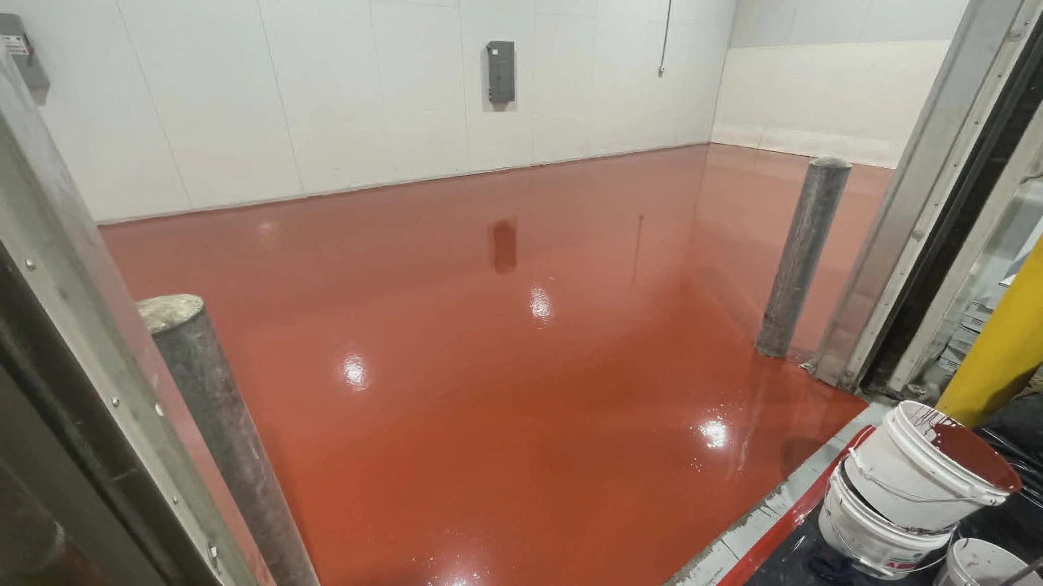 A freshly painted red floor inside an elevator shaft with some paint buckets and tools along the sides.