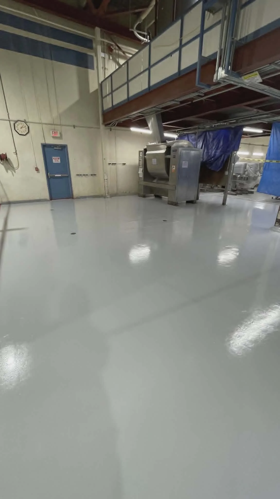 Empty industrial or warehouse space with shiny painted concrete floor, some equipment and a staircase with blue safety railing.