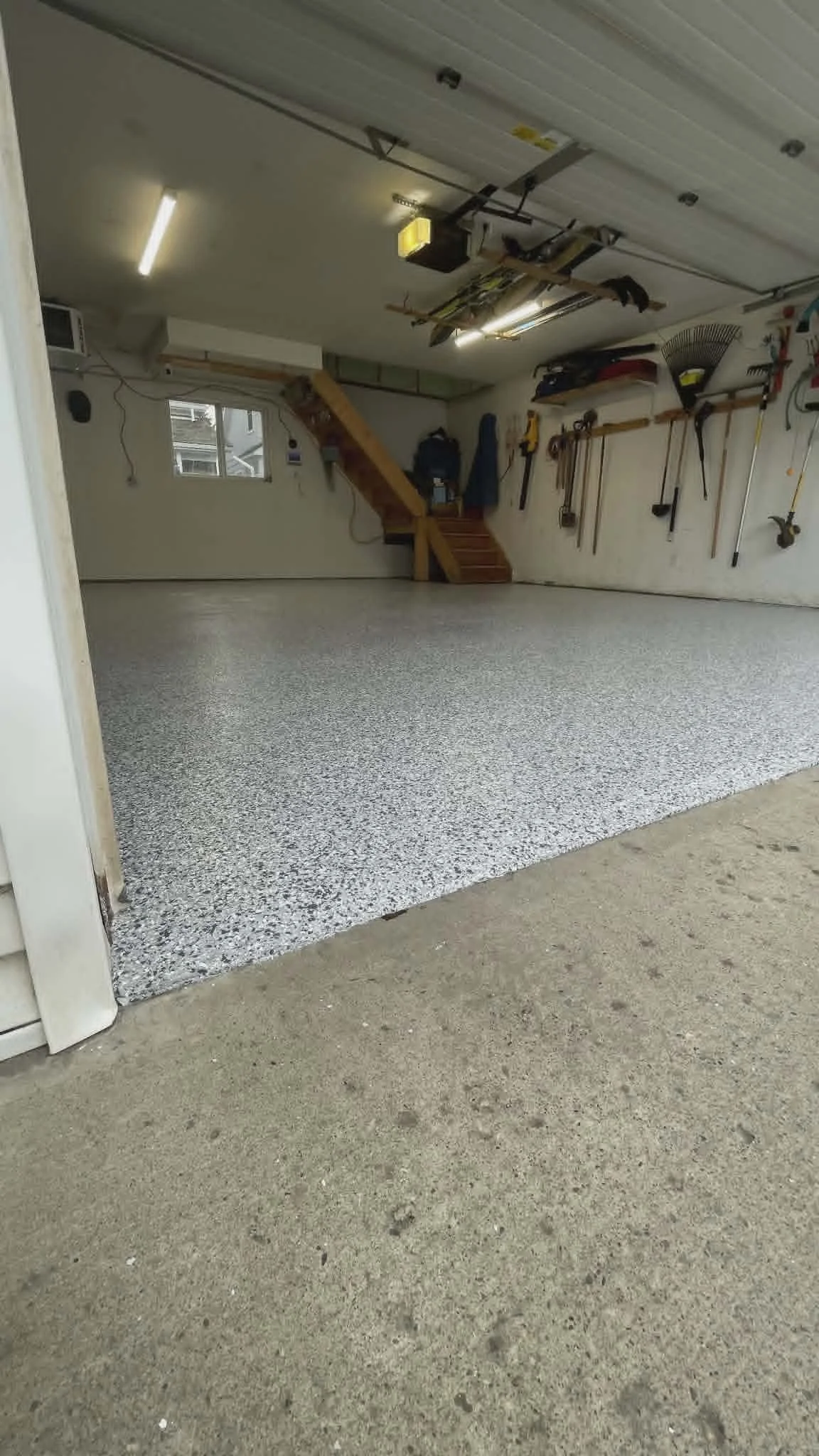 A garage with a fresh coat of light-colored epoxy flooring, tools hanging on a wall, and a small window.