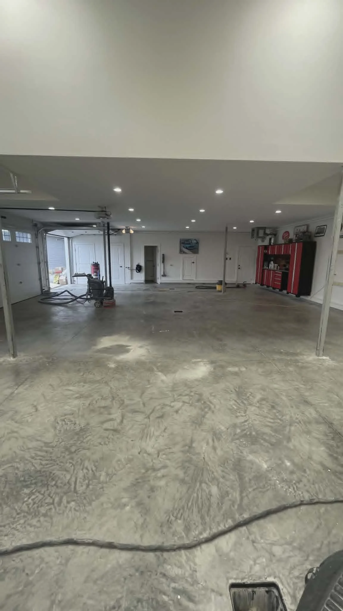 Clean, empty garage with bright ceiling lights, red tool cabinet, and some tools and equipment, including a wet vacuum or shop vac and a fire extinguisher.