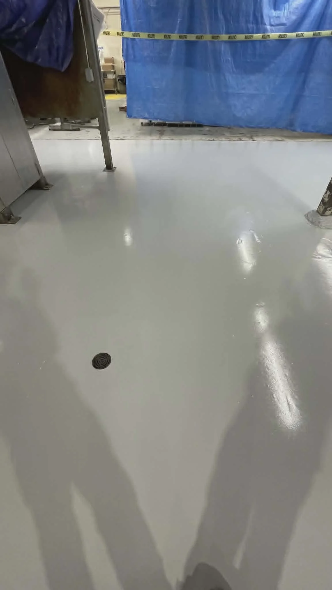 Clean, shiny white floor with shadows of people and a drain in the middle.