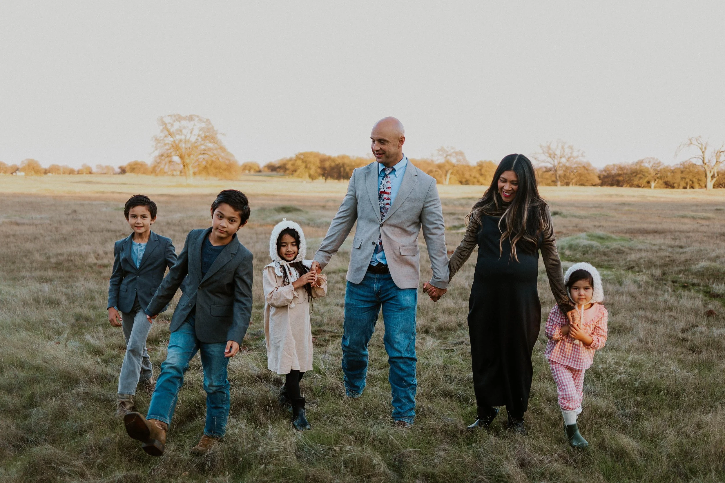 A group of six people, including children and adults, walking hand in hand in an open grassy field during the daytime.