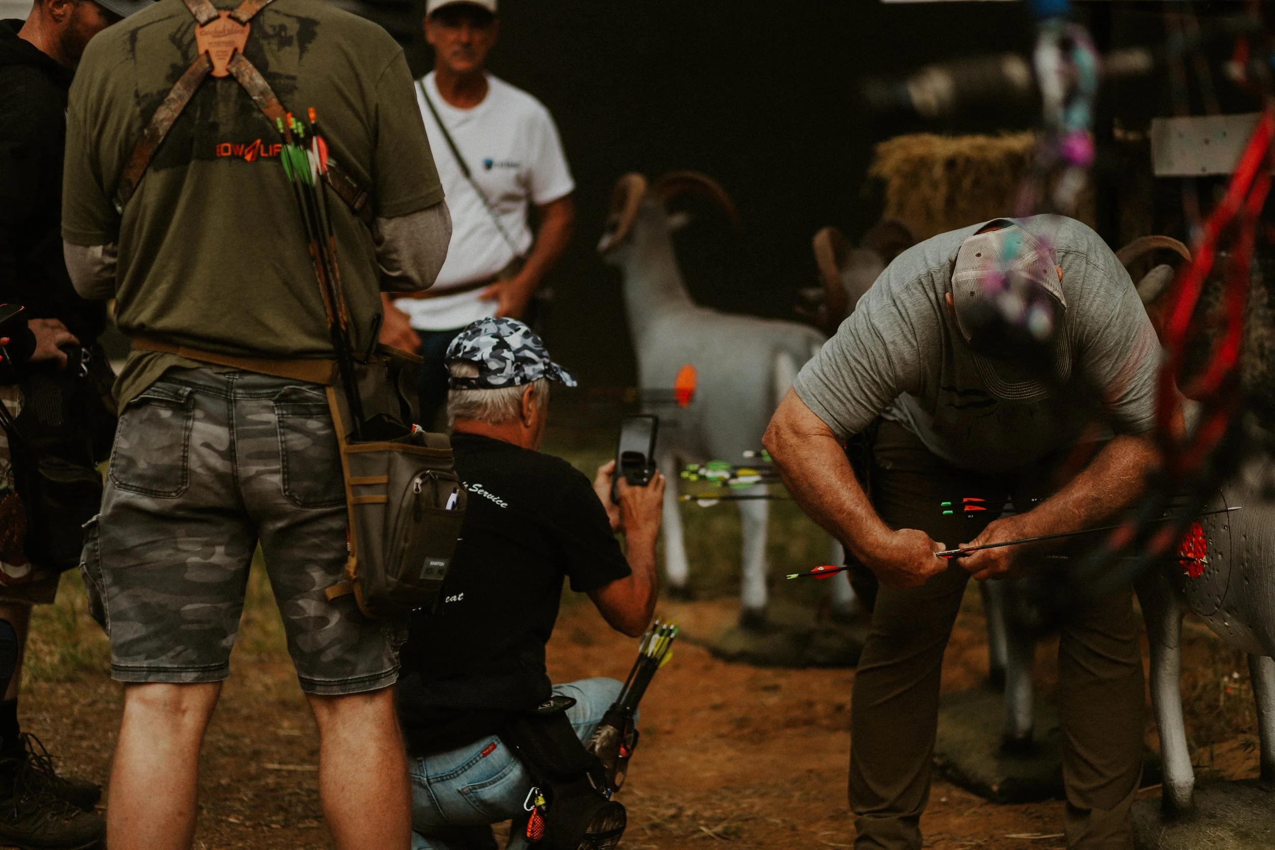 Group of men preparing archery equipment outdoors, with arrows and bows visible, during dusk or evening.