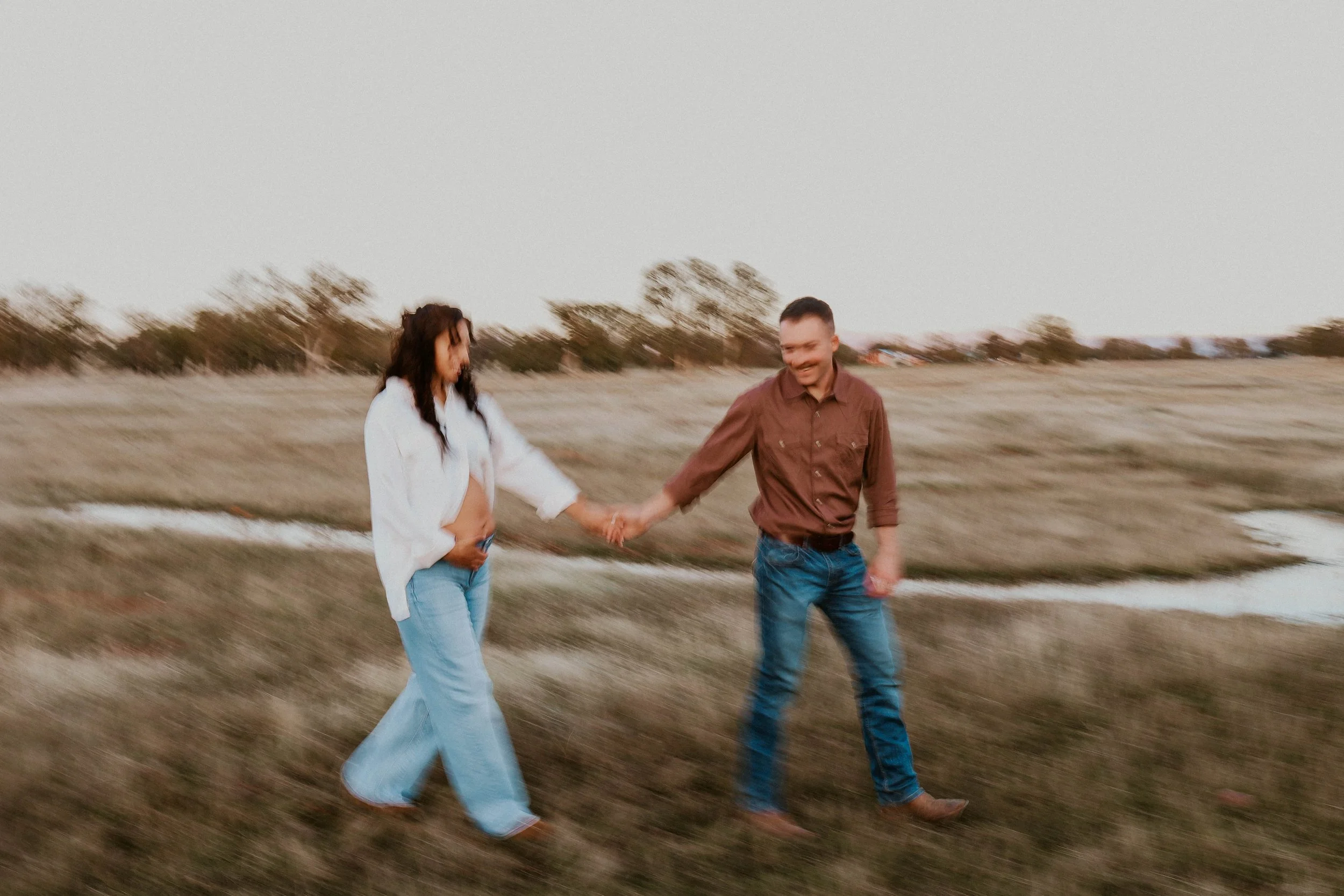 A couple holding hands and walking in a field during sunset.