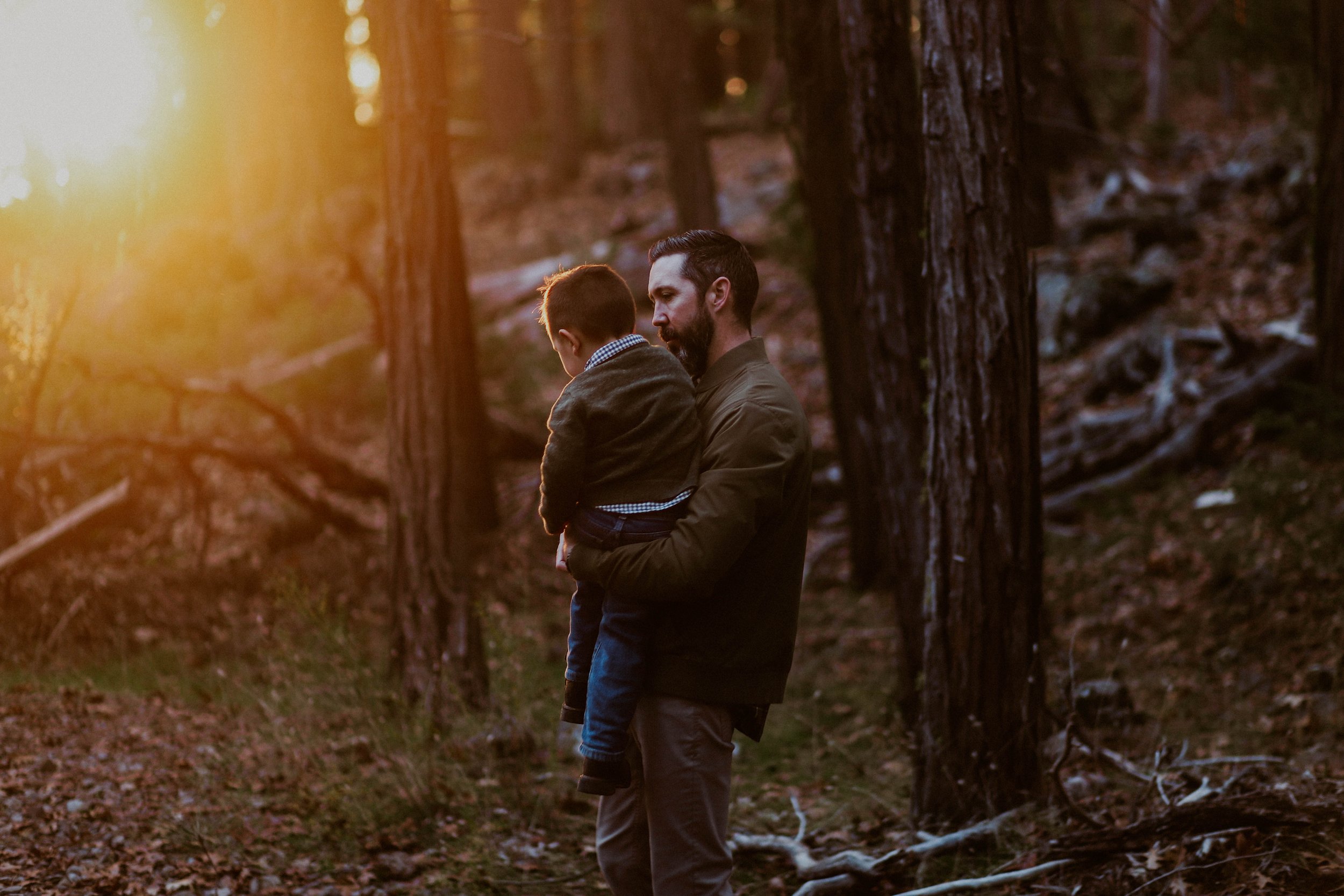 A man holding a child in a forest during sunset.