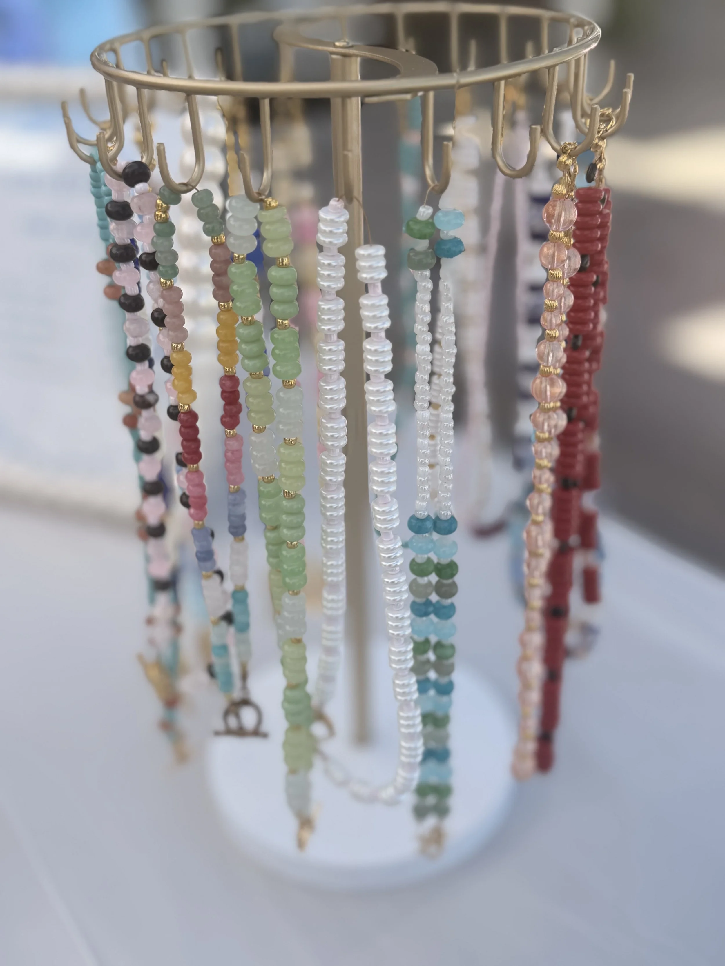 Colorful beaded jewelry hanging from a rotational display rack with hooks.