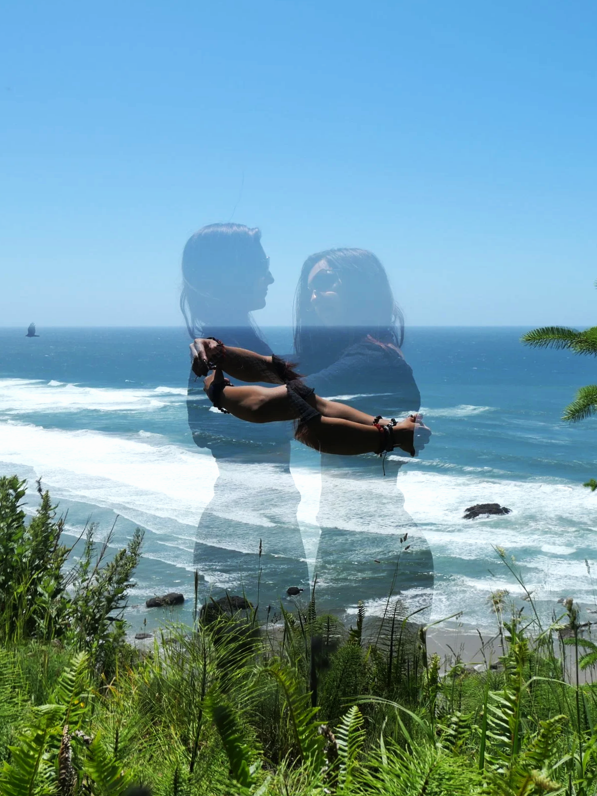 A double exposure photograph of a woman practicing yoga on a grassy coastline with the ocean in the background, and her silhouette overlaid with an image of two women facing each other.