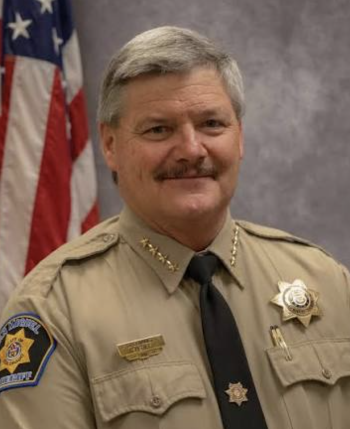 Smiling man in a sheriff uniform and an American flag
