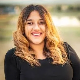 A woman with curly brown hair smiling outdoors.