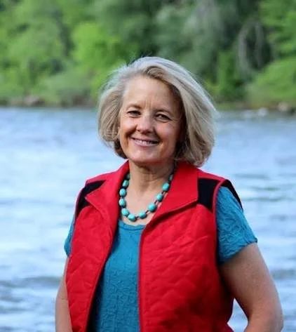 Smiling woman by a river wearing a red vest