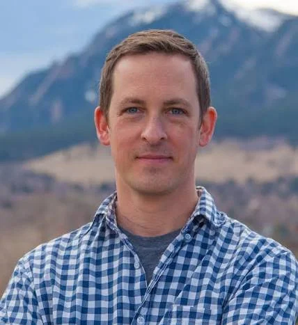 man with blue checked shirt in front of mountain