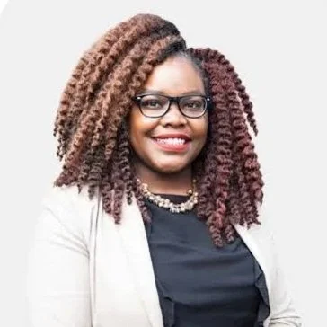 Portrait of a smiling Black woman with glasses and curly hair, wearing a white blazer and black top.
