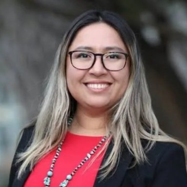 A woman with long, blonde hair wearing glasses, a red top, and a black blazer, smiling outdoors.