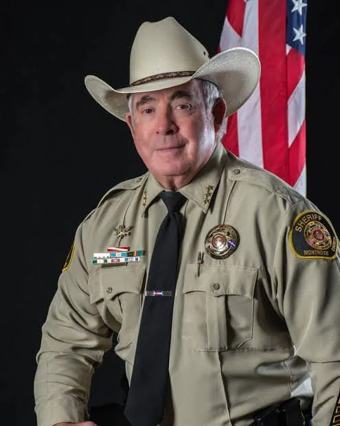Man in a sheriff uniform and cowboy hat in front of an americna flag