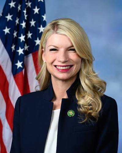 Smiling women with blonde hair in front of a US flag.