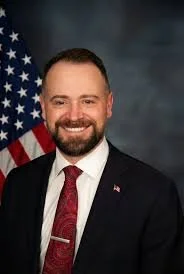 Smiling man with a burgundy tie in front of an American flag