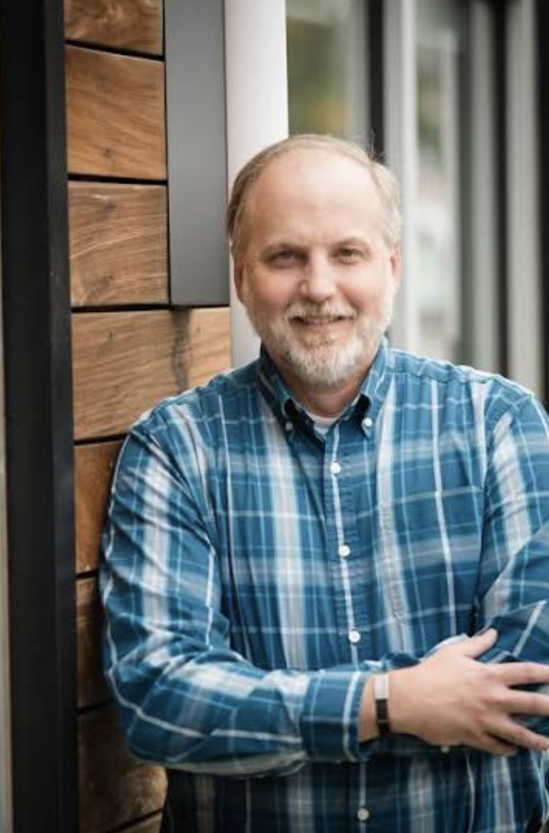 Smiling man with a white beard wearing a blue plaid shirt