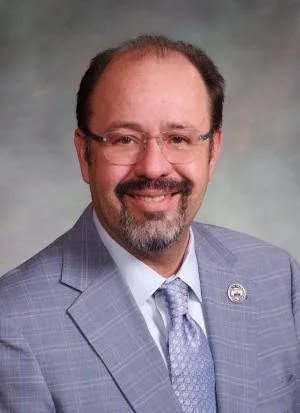 smiling man with a gray suit wearing glasses and has a goattee