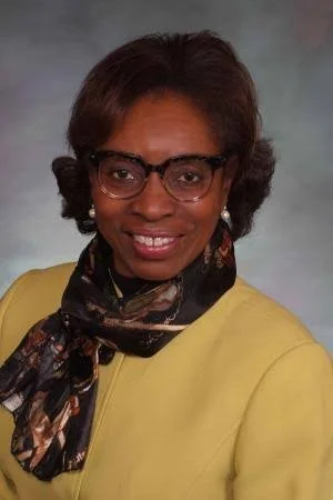 Woman with short black hair, glasses, and a yellow sweater